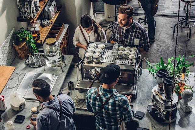 Two people buying a coffee at a hipster cafe while the baristas processing the order.