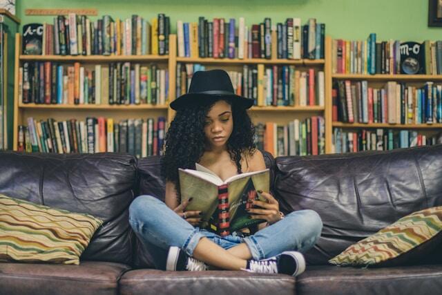 Woman engrossed and reading book sitting cross legged black leather couch