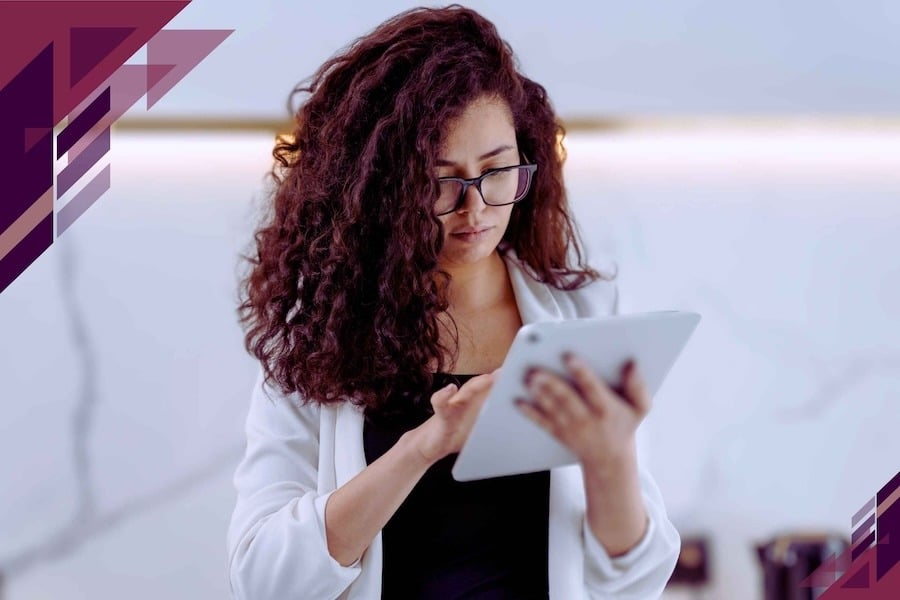 A woman with curly black hair and black glasses standing up and swiping on her tablet.